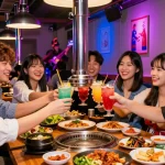 A group of friends celebrating at 상봉동 한국관나이트 with cocktails and Korean BBQ, illuminated by vibrant neon lights.
